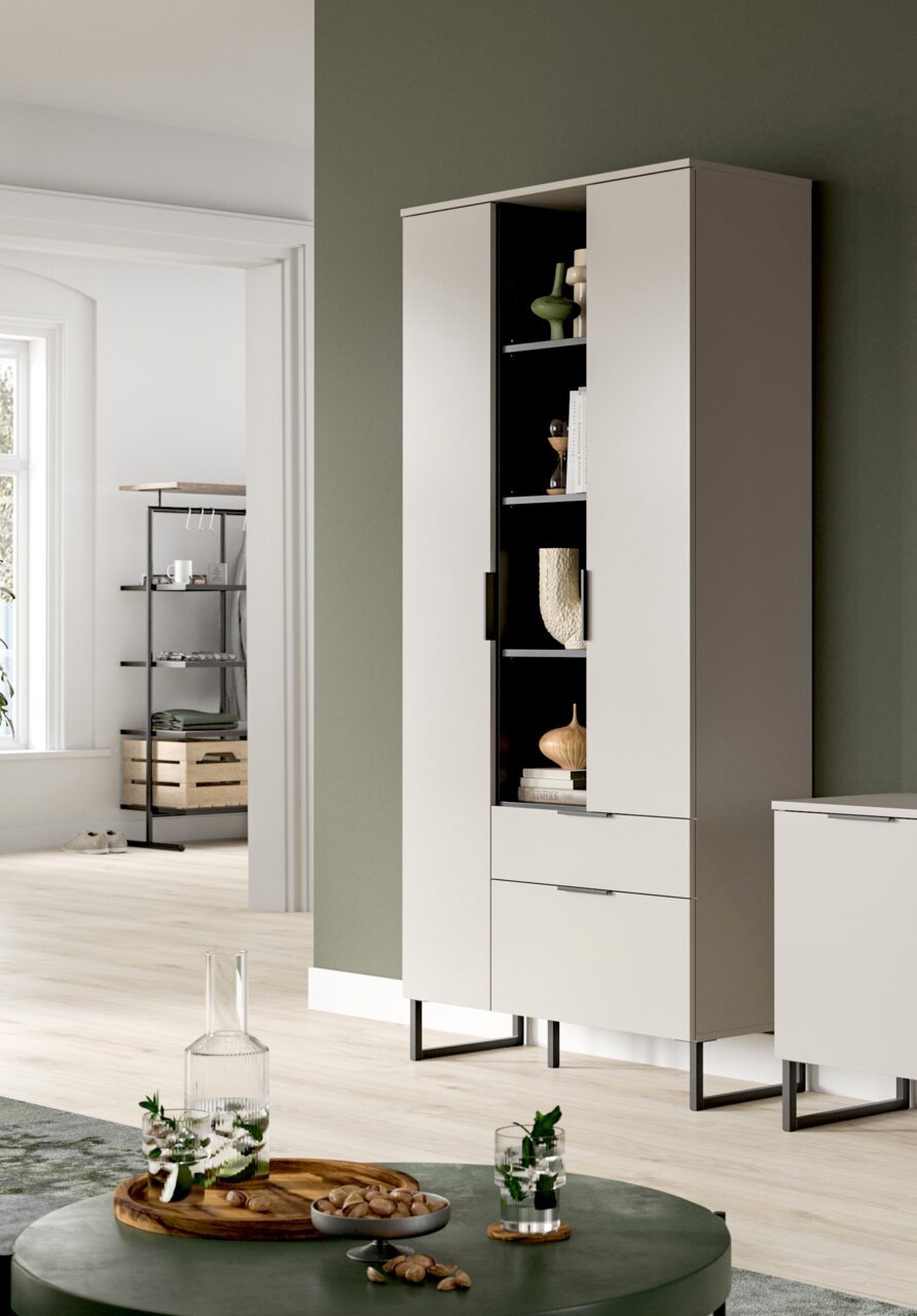 MID.YOU Stauraumtype NOIDA Moderner hoher Wohnzimmerschrank in Hellgrau mit schwarzen Metallfüßen, zwei Türen und Schublade, eine Tür geöffnet mit sichtbaren Regalfächern und Deko, in heller Wohnraum-Szene; Perspektive: leicht schräg von vorn/rechts.