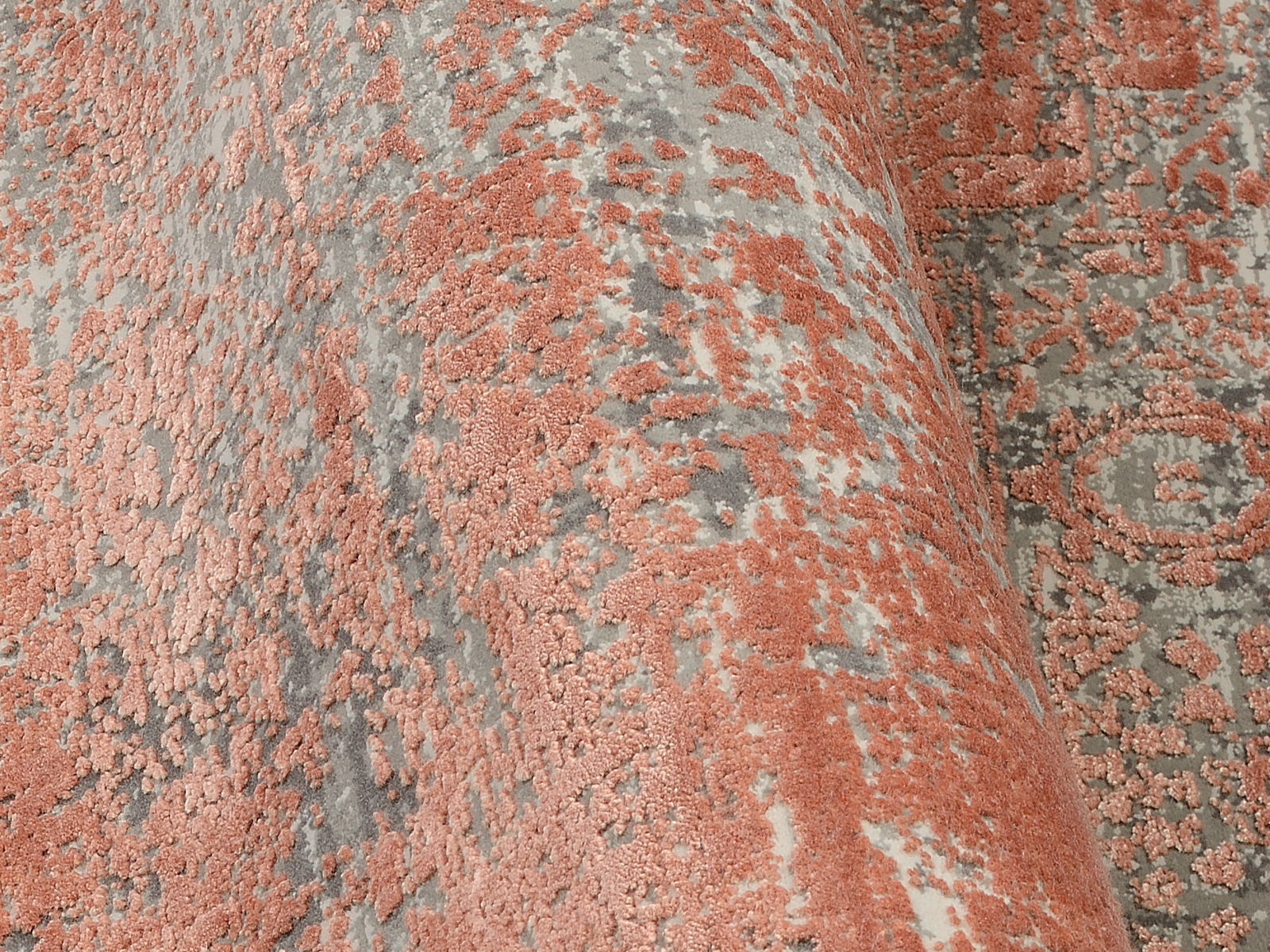 Nahaufnahme eines Designer-Teppichs mit abstraktem Muster in Rot- und Grautönen, perspektivisch von der Seite aufgenommen.