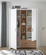 Zweiflügeliger Drehtürenschrank in Weiß mit Holzelementen, geöffnet, mit Regalen und Schubladen, gefüllt mit Kleidung und Dekorationen, aus frontaler Perspektive.