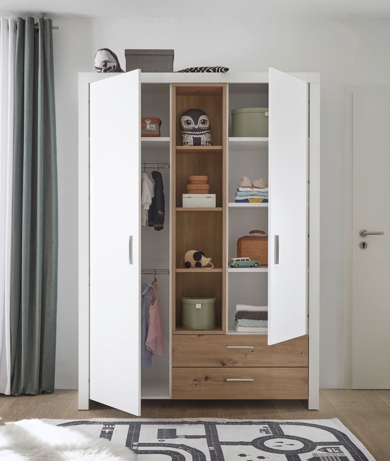 Zweiflügeliger Drehtürenschrank in Weiß mit Holzelementen, geöffnet, mit Regalen und Schubladen, gefüllt mit Kleidung und Dekorationen, aus frontaler Perspektive.