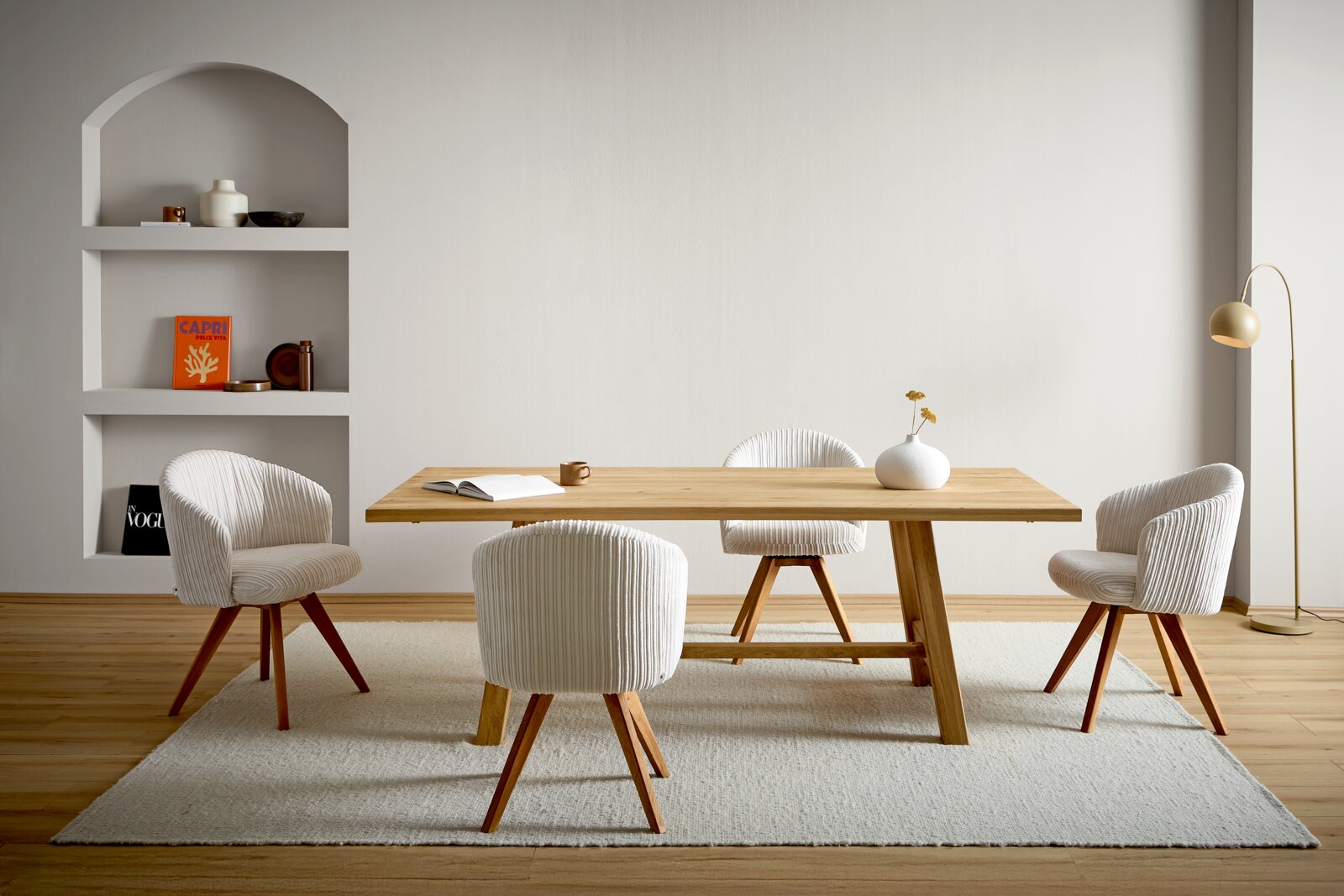 Linea Natura Esstisch HAMBURG Modernes Esszimmer mit rechteckigem Holztisch und vier gepolsterten, gerippten Stühlen in Creme auf hellem Teppich, seitliche Perspektive auf Tisch und Sitzgruppe vor heller Wand mit Regalnische und Stehlampe
