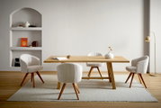Modernes Esszimmer mit rechteckigem Holztisch und vier gepolsterten, gerippten Stühlen in Creme auf hellem Teppich, seitliche Perspektive auf Tisch und Sitzgruppe vor heller Wand mit Regalnische und Stehlampe