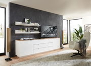 Modernes TV-Sideboard in einem stilvollen Wohnzimmer, seitliche Perspektive. Das Sideboard ist weiß mit einer Holzoberfläche und bietet Platz für einen großen Fernseher. Dekorative Regale und Pflanzen ergänzen das elegante Design.