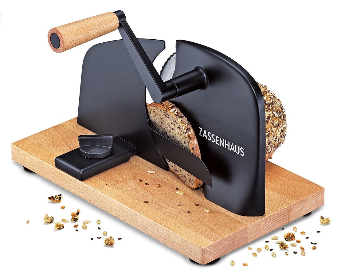 Zassenhaus Brotschneidemaschine PURE Manuelle Brotschneidemaschine mit Holzsockel und schwarzem Metallgehäuse, ZASSENHAUS, mit Kurbel und eingespanntem Körnerbrot, schräg von vorn rechts fotografiert