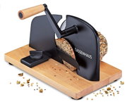 Manuelle Brotschneidemaschine mit Holzsockel und schwarzem Metallgehäuse, ZASSENHAUS, mit Kurbel und eingespanntem Körnerbrot, schräg von vorn rechts fotografiert