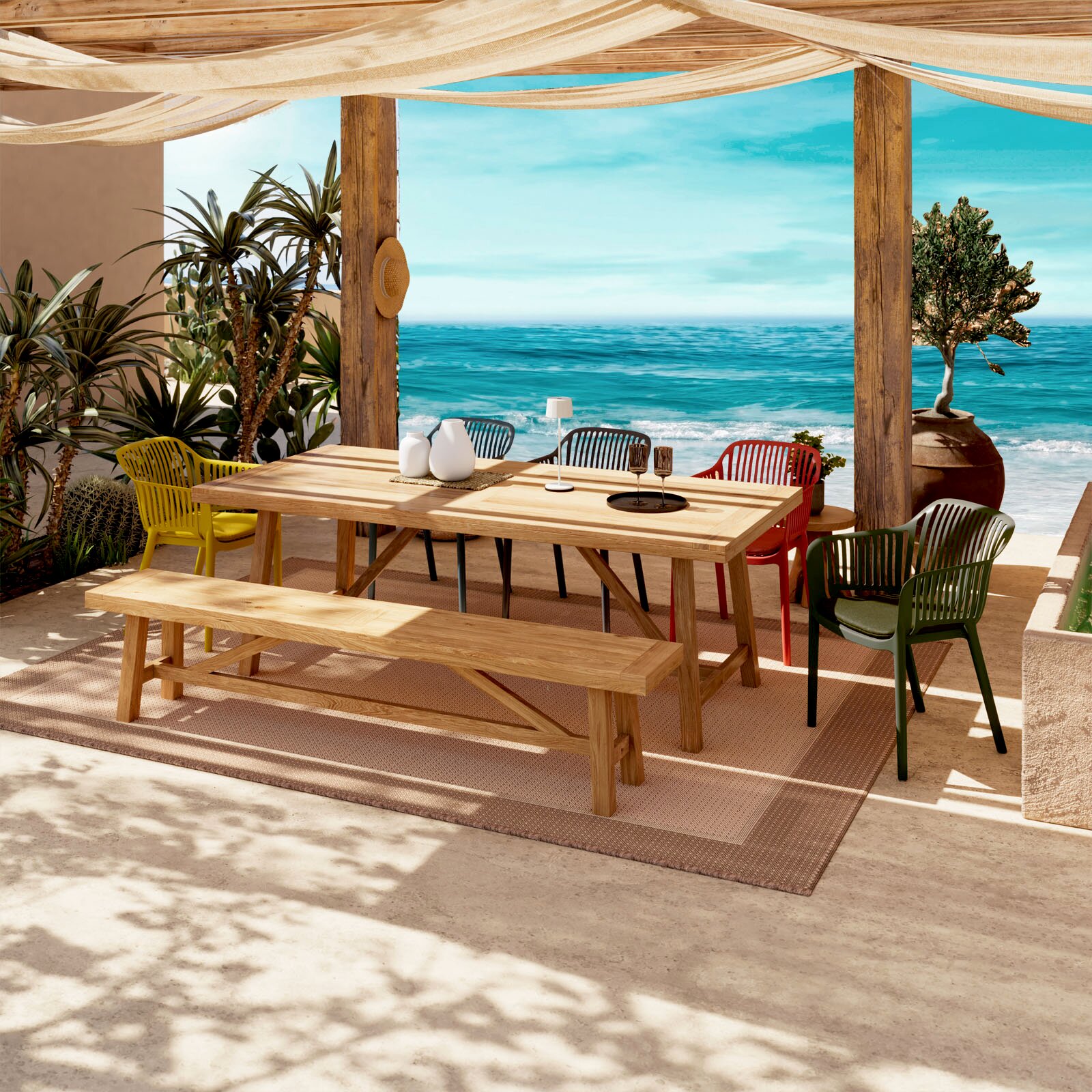 Ambia Garden Stapelsessel MINO Großer Outdoor-Esstisch aus hellem Holz mit passender Bank und farbigen Gartenstühlen auf einer überdachten Terrasse am Meer, Frontansicht in leichter Seitenperspektive