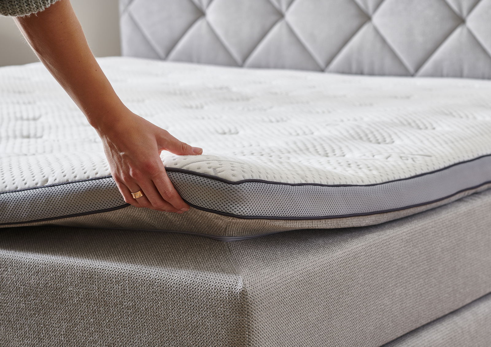 Nahaufnahme eines Boxspringbetts mit einer Hand, die die Matratze anhebt, um die Struktur und den Komfort zu zeigen.