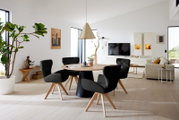 Moderne fauteuil met zwarte bekleding en houten poten, in een stijlvol ingerichte woonkamer met uitzicht op de eettafel.