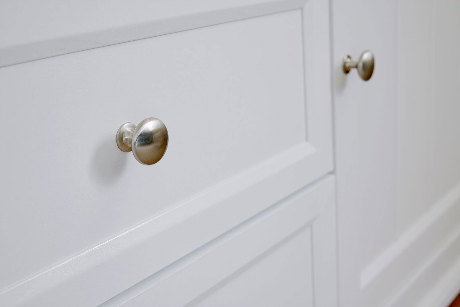 Nahaufnahme eines weißen Sideboards mit silbernen Knöpfen, seitliche Perspektive