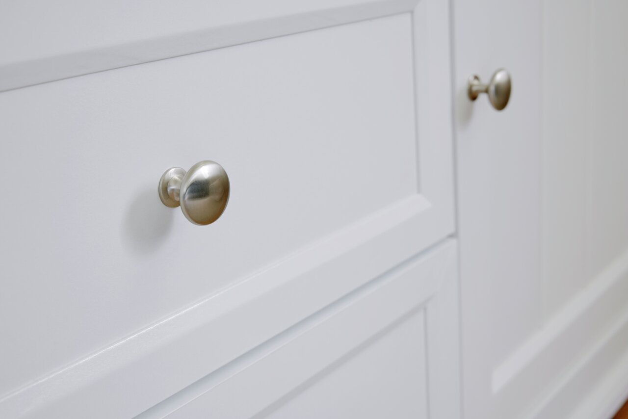 Nahaufnahme eines weißen Sideboards mit silbernen Knöpfen, seitliche Perspektive