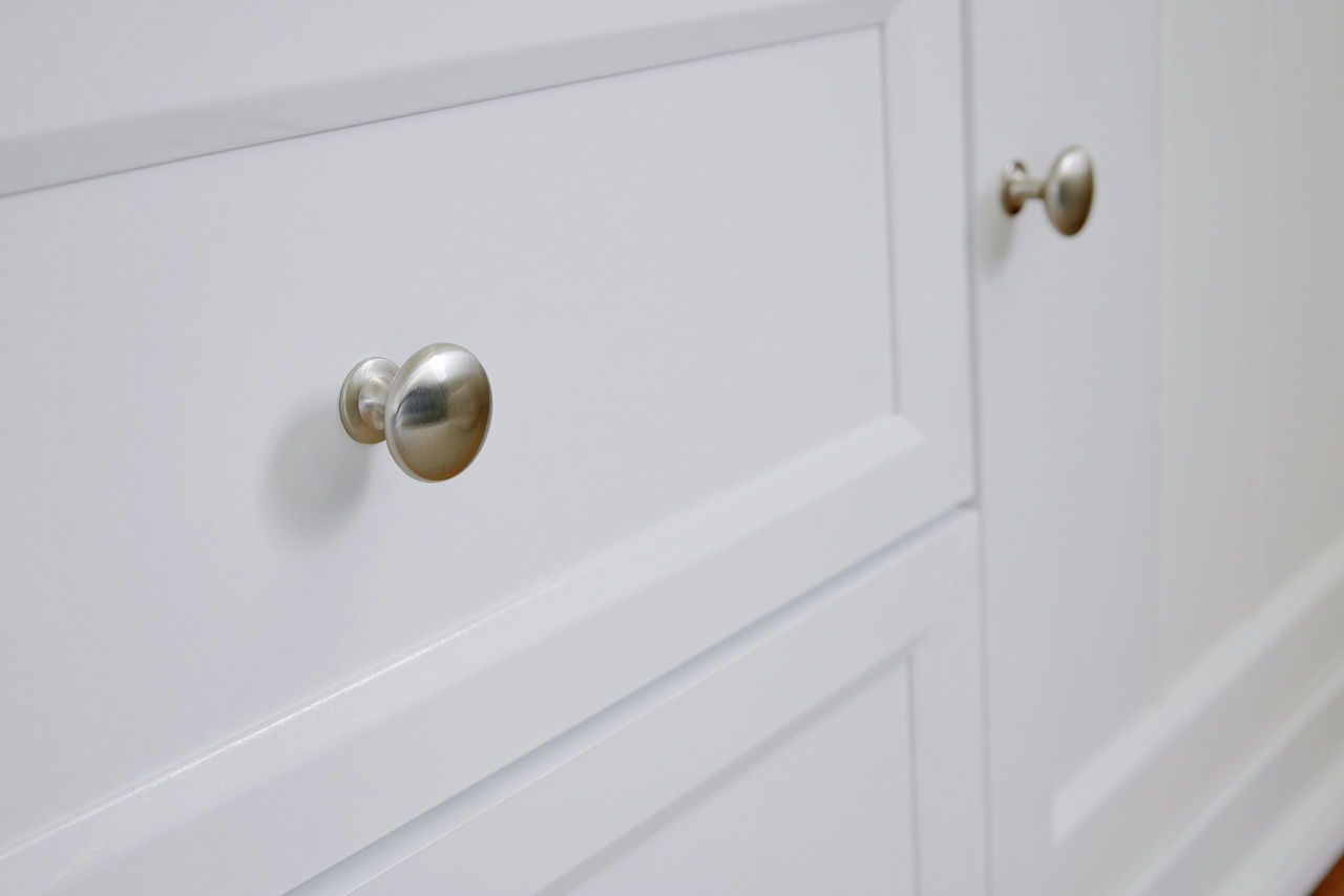 Nahaufnahme eines weißen Sideboards mit silbernen Knöpfen, seitliche Perspektive