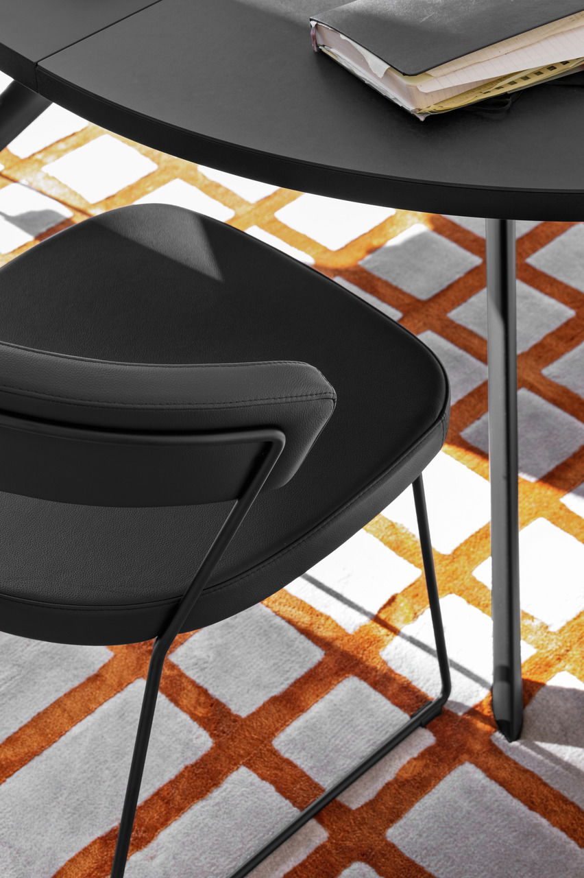 Moderner schwarzer Stuhl mit Metallgestell, von oben fotografiert, auf einem Teppich mit orange-weißem Muster.