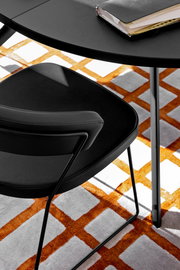 Moderner schwarzer Stuhl mit Metallgestell, von oben fotografiert, auf einem Teppich mit orange-weißem Muster.