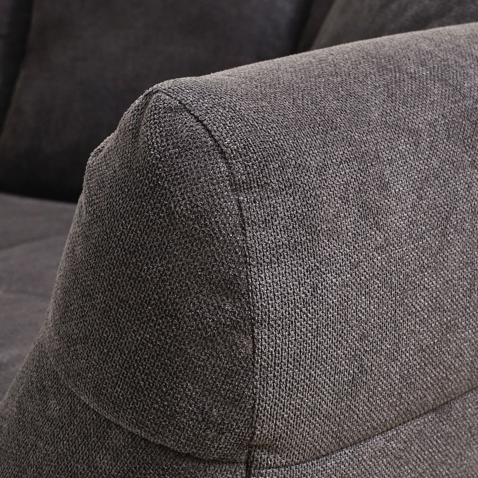 Nahaufnahme eines grauen Big-Sofas mit strukturiertem Stoffbezug, seitliche Perspektive auf die Armlehne.