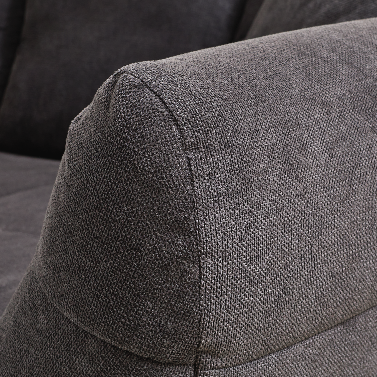 Nahaufnahme eines grauen Big-Sofas mit strukturiertem Stoffbezug, seitliche Perspektive auf die Armlehne.