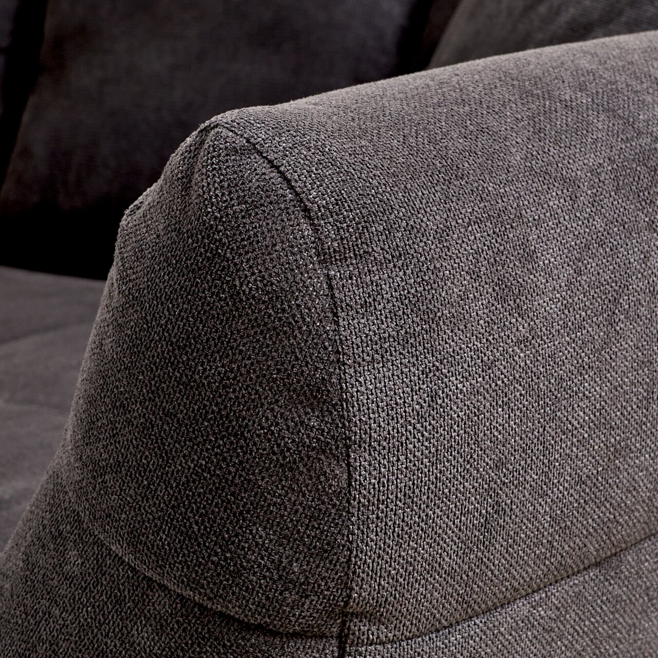 Nahaufnahme eines grauen Big-Sofas mit strukturiertem Stoffbezug, seitliche Perspektive auf die Armlehne.