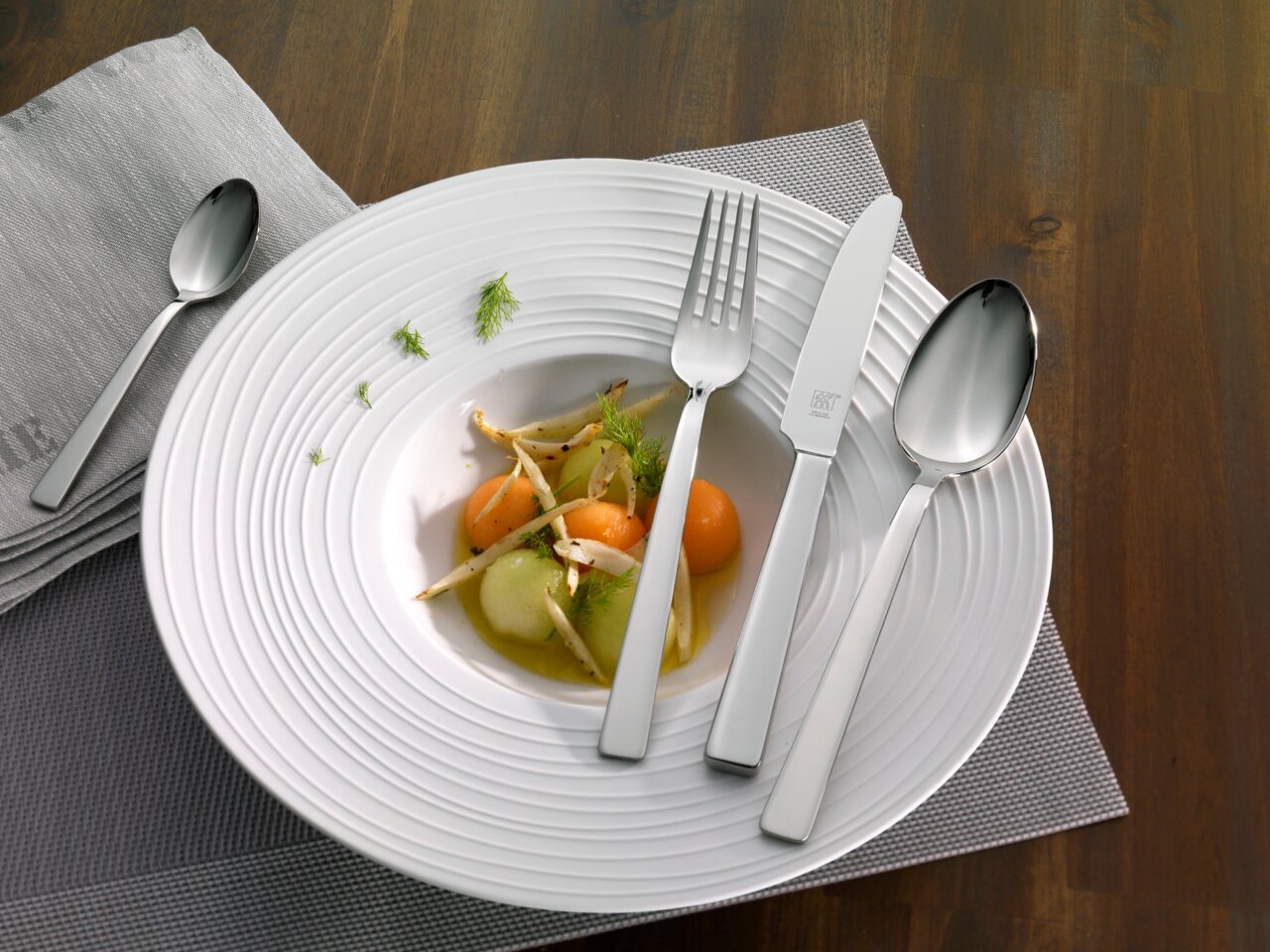 Elegante bestekset King (100-delig) op een gedekte tafel met bord en servet, gezien van bovenaf.