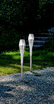 Zwei moderne Solarleuchten aus Edelstahl und Kunststoff, aufgestellt in einem Garten mit Kiesweg und Treppen im Hintergrund, seitliche Perspektive.