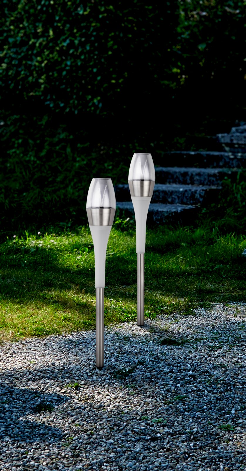 Zwei moderne Solarleuchten aus Edelstahl und Kunststoff, aufgestellt in einem Garten mit Kiesweg und Treppen im Hintergrund, seitliche Perspektive.