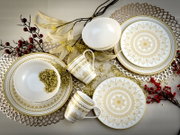 Draufsicht auf elegantes weißes Geschirrset mit goldfarbenem Mandala-Dekor (Teller, Schalen und Tassen) dekorativ arrangiert auf Tischunterlage mit Beerenzweigen.