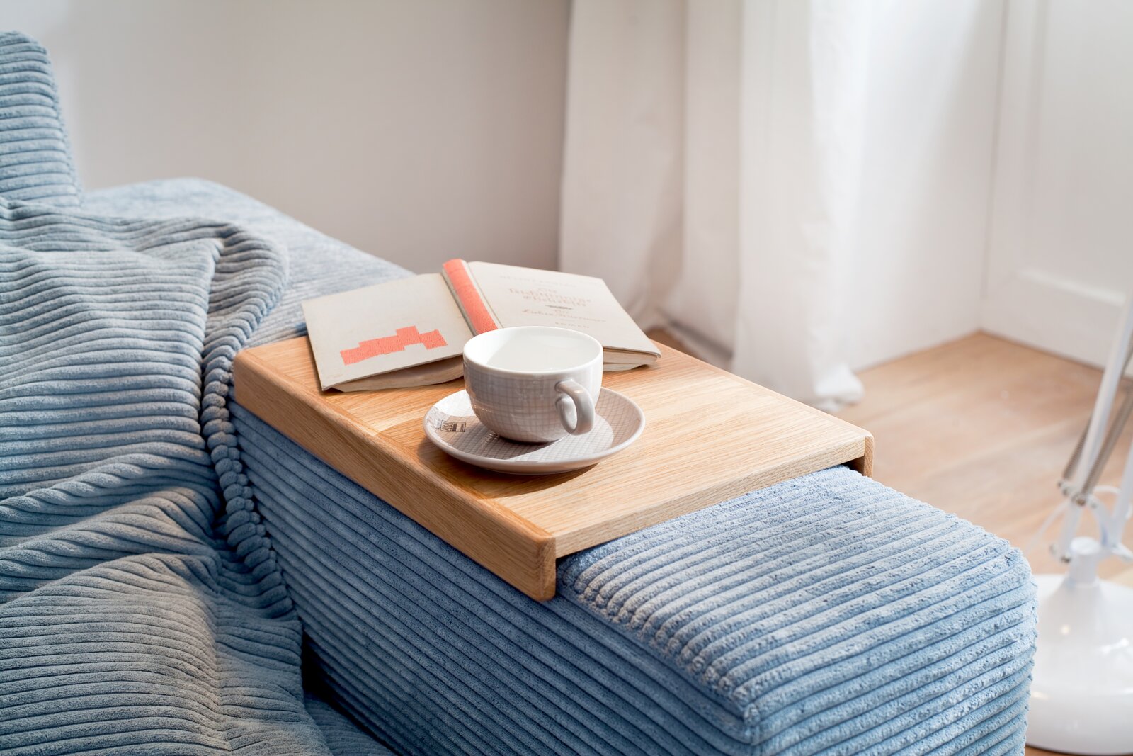 Holztablett auf der Armlehne eines Sofas mit einer Tasse und einem Buch, seitliche Perspektive