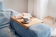 Holztablett auf der Armlehne eines Sofas mit einer Tasse und einem Buch, seitliche Perspektive