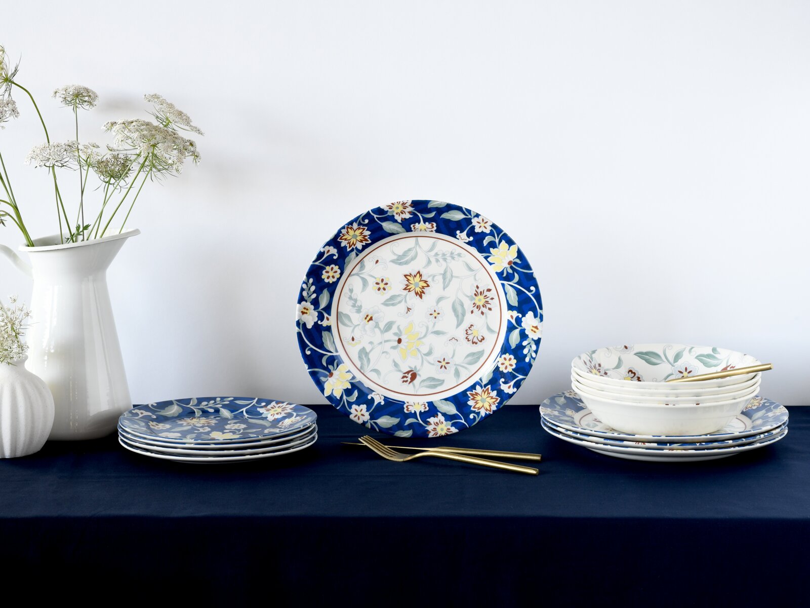 creaTable Tellerset 12-tlg ODESSA Florales Porzellan-Geschirrset mit blauem Rand: Teller und Schalen auf dunkelblauem Tisch, ein großer Teller frontal im Mittelpunkt, seitliche Perspektive mit leichtem Blick von vorn