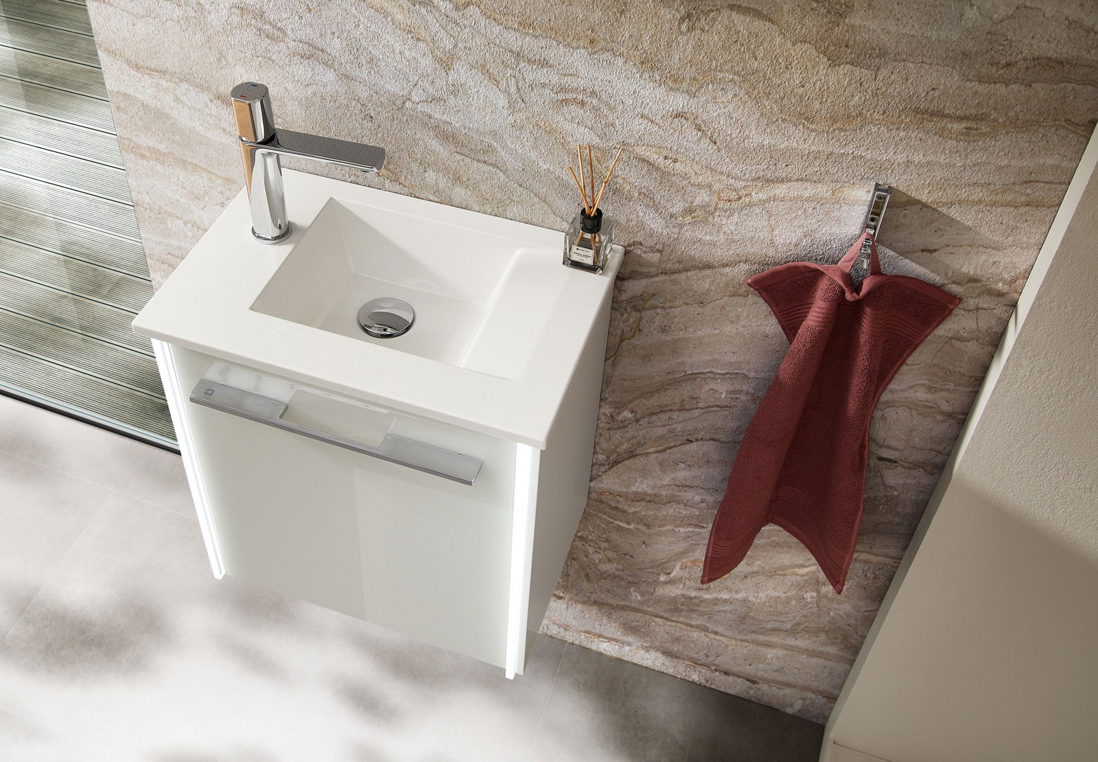 Moderne Waschbecken-Einheit mit weißem Unterschrank und Chromarmatur, von oben betrachtet, neben einem roten Handtuch an der Wand.