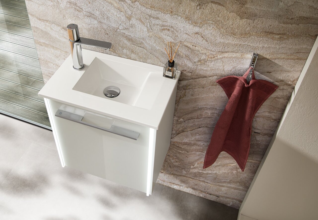 Moderne Waschbecken-Einheit mit weißem Unterschrank und Chromarmatur, von oben betrachtet, neben einem roten Handtuch an der Wand.
