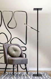 Schwarze Stehleuchte in modernem Design, neben einem grauen Stuhl mit runder Kissenlehne, vor einer abstrakten Wandkunst. Seitliche Perspektive.