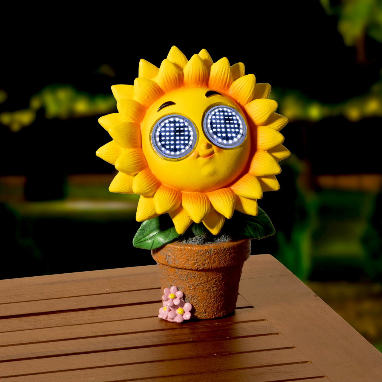 Frontalansicht einer Solarfigur in Form einer Sonnenblume mit leuchtenden Augen, die in einem Blumentopf auf einem Holztisch steht.