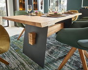 Moderner Esstisch aus Holz mit schwarzem Metallgestell, gedeckt mit Geschirr und Weingläsern, seitliche Perspektive.