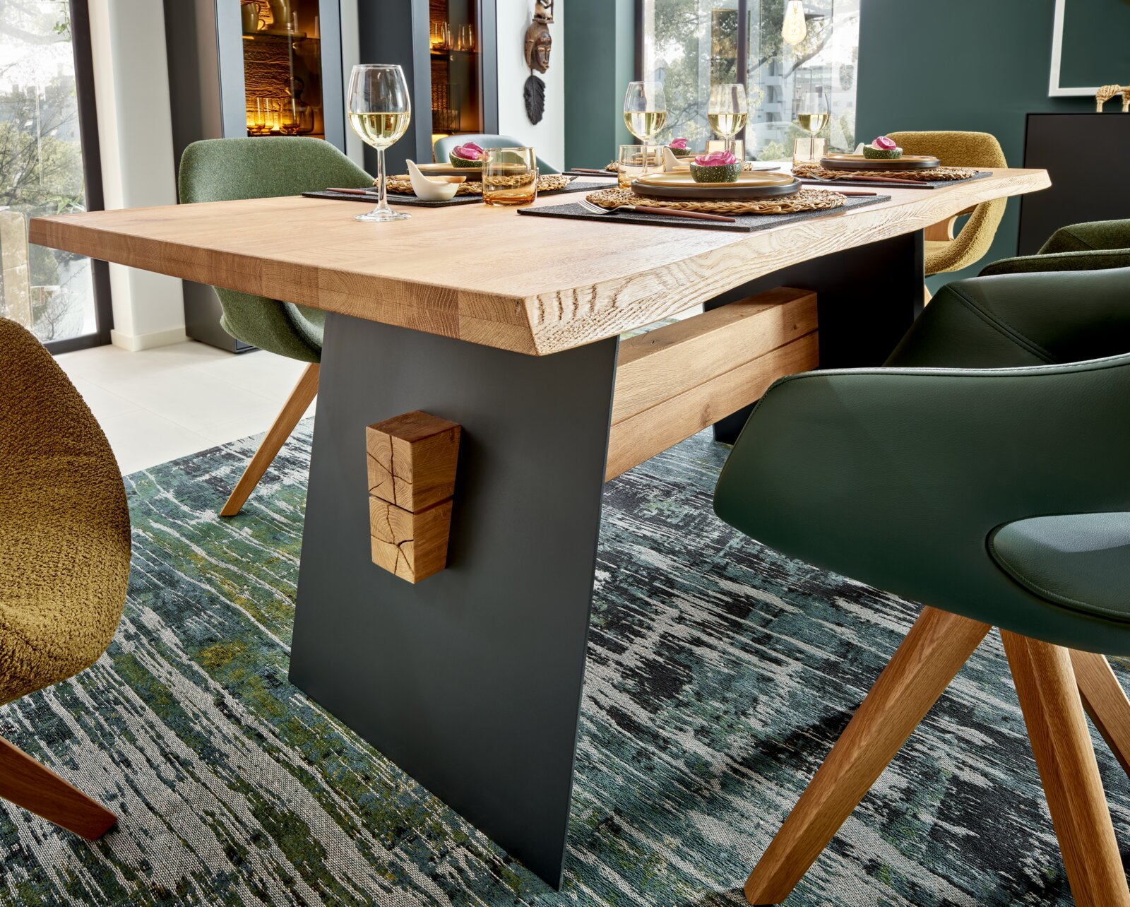 Moderne houten eettafel met een zwart metalen onderstel, gedekt met serviesgoed en wijnglazen, zijaanzicht.
