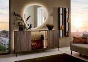 Moderne wandspiegel met organische vorm, verlicht, boven een stijlvol dressoir in een elegante woonkamer met uitzicht op de stad bij zonsondergang.