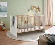 Modernes Babybett/Kinderbett aus hellem Holz mit weißen Seitenteilen und Holzsprossen im Kinderzimmer, seitliche Perspektive schräg von vorn