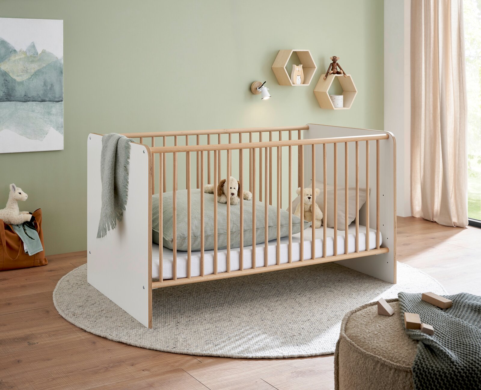 MyBaby Babybett ASTEA Modernes Babybett/Kinderbett aus hellem Holz mit weißen Seitenteilen und Holzsprossen im Kinderzimmer, seitliche Perspektive schräg von vorn