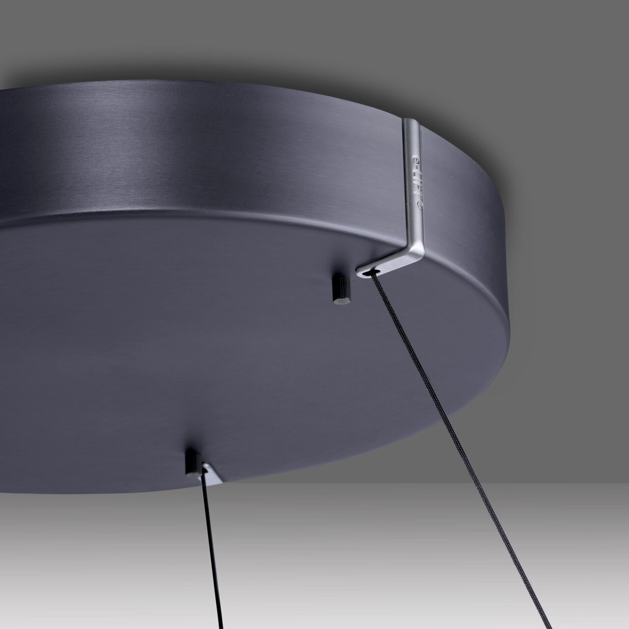 Nahaufnahme der Unterseite einer modernen, runden Pendelleuchte in mattem Schwarz mit zwei Kabeln, die von der Decke hängen.