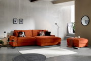 Moderne oranje hoekbank met brede chaise longue en bijpassende poef in een minimalistische woonkamer, vooraanzicht licht van links