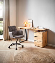 Moderner Schreibtisch aus Holz mit schwarzem Metallgestell, seitlich von einem grauen Bürostuhl und einer kleinen Tischlampe begleitet, in einem hellen Raum mit Holzboden und natürlichem Licht.