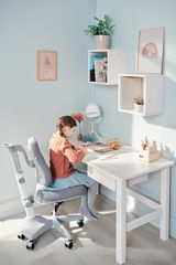 Kind sitzt auf einem ergonomischen Schreibtischstuhl an einem weißen Schreibtisch, Seitenansicht