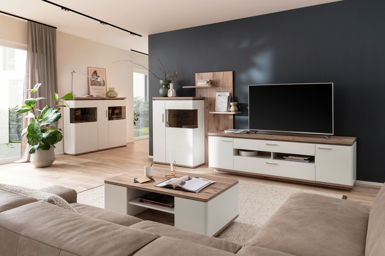 Moderne Wohnzimmer-Wandkombination in hellem Holz und Weiß, mit TV-Schrank, Vitrine und Regal, aus der Perspektive eines gemütlichen Wohnzimmers mit Sofa und Couchtisch.