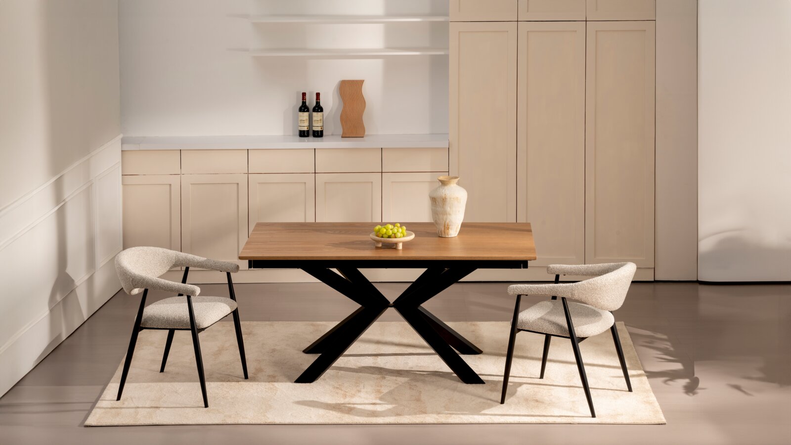 Moderner Esstisch aus Holz mit schwarzem X-förmigem Gestell, dekoriert mit Vase und Schale Trauben, flankiert von zwei gepolsterten Stühlen; frontale Perspektive auf das Set in hellem Wohnraum.