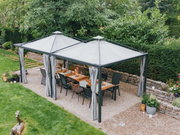 Luchtfoto van een elegante tuinpagode met gordijnen, met daaronder een eettafel met stoelen, omgeven door weelderige begroeiing.