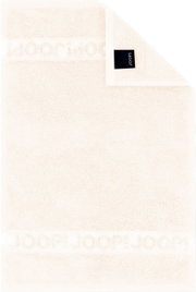 Cremefarbenes JOOP! Frottierhandtuch mit eingewebtem Logo-Bordürenstreifen und schwarzem Markenlabel, flach von oben fotografiert (Draufsicht)