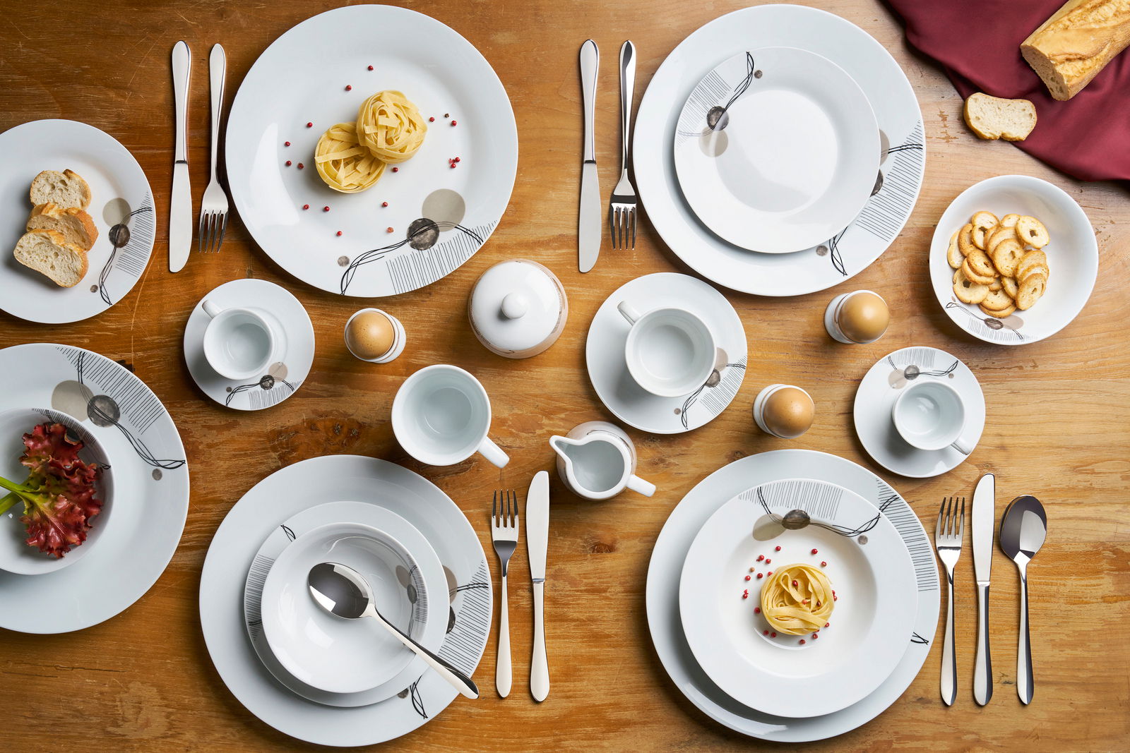 Van Well Kombiservice 62 tlg. ALBERTA Vogelperspektive auf ein stilvolles 62-teiliges Kombiservice-Set mit modernem Design auf einem Holztisch, inklusive Teller, Tassen, Besteck und Schalen, dekoriert mit Speisen.