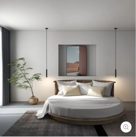 Modernes Schlafzimmer mit rundem Holzbett und weißer Bettwäsche, zwei schlanken schwarzen Pendelleuchten, großem Teppich, Pflanze im Topf und Wandbild; Frontalansicht auf das Bett aus leicht erhöhter Perspektive.