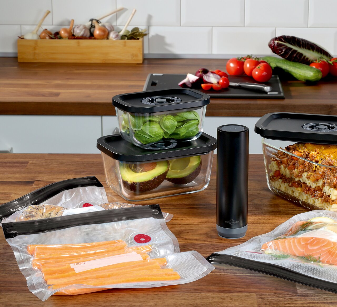 Vakuumier-Set EASYFRESH, 7-tlg, bestehend aus Vakuumbehältern und -beuteln, auf einer Küchenarbeitsplatte präsentiert, mit frischen Lebensmitteln wie Avocado, Salat und Lachs, seitliche Perspektive.