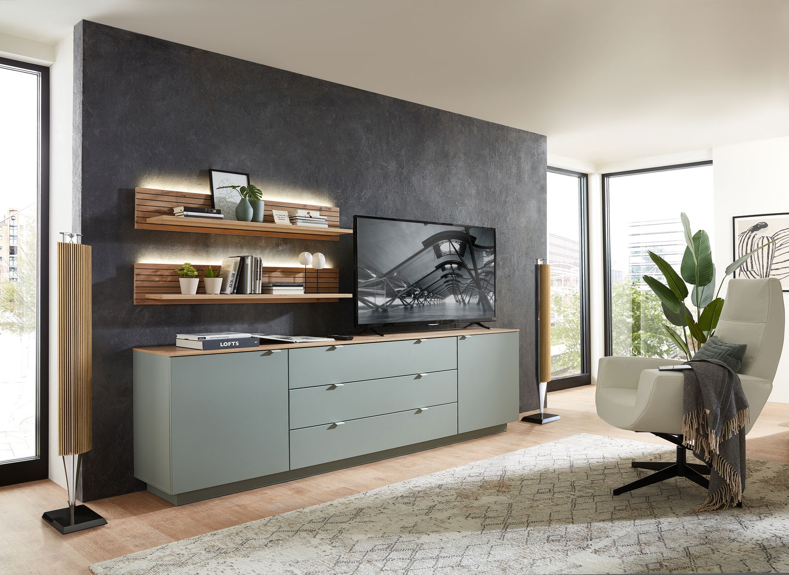 Modernes Wohnzimmer mit Wandboard CORE, das an einer dunklen Wand montiert ist, mit Dekorationen und Beleuchtung. Perspektive von der Seite.