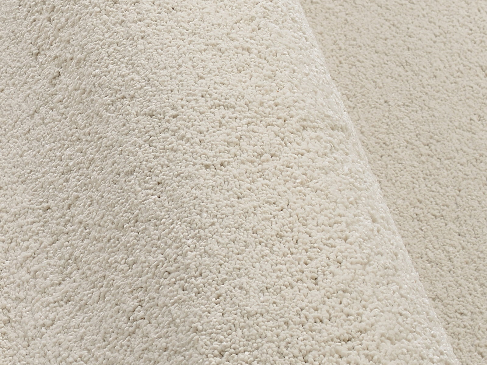 Nahaufnahme eines cremefarbenen Uni-Teppichs mit weicher, flauschiger Textur, seitliche Perspektive