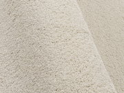 Nahaufnahme eines cremefarbenen Uni-Teppichs mit weicher, flauschiger Textur, seitliche Perspektive